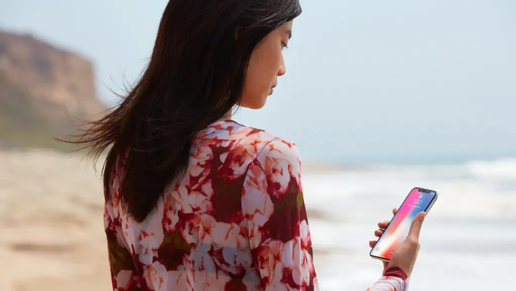 Face recognition. A woman standing by the sea, holding showing her phone towards her face for face recognition.