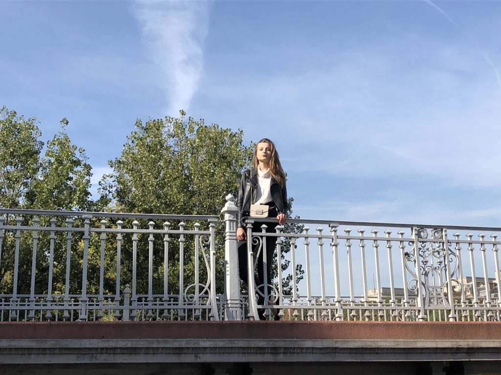 A photo of a woman standing on a bridge in front of tree taken by iPhone 8