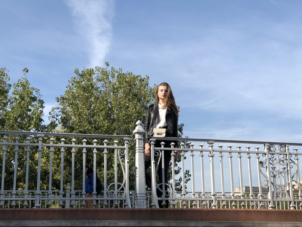 A photo of a woman standing on a bridge in front of tree taken by iPhone 8 plus.